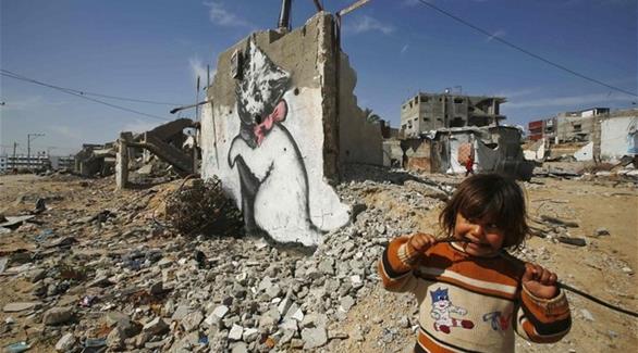 فتاة فلسطينية تنظر للوحة جدارية رسمها الفنان بانكسي في غزة، إبان العمليات الإسرائيلية نهاية 2014 على غزة(رويترز)