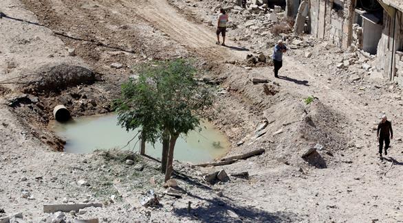 سوريون يعبرون بالقرب من حفرة امتلأت بالماء بعد غارات كثيفة على حلب(رويترز)
