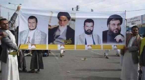 عنصران من الحوثيين يرفعان لافتة عليها صور لقادة شيعة بينهم زعيم جماعة الحوثيين (المصدر أونلاين)