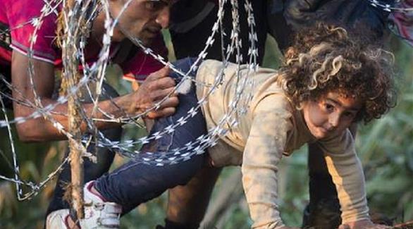أب سوري يدفع بطفلته من تحت سياج شائك لدخول الحدود الأوروبية (أرشيف)
