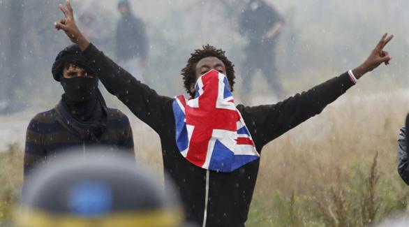 متظاهر يحمل العلم البريطاني أثناء هروبه من الدخان المسيل للدموع في كاليه، فرنسا (رويترز)
