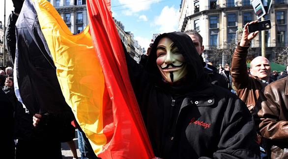 متظاهر يرتدي قناع "غي فوكس" ويرفع العلم البلجيكي