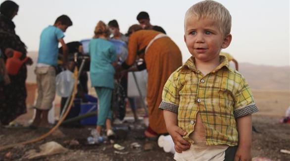 طفل يقف امام أهله اللاجئين الذين يحاولون الحصول على المياه (أحمد يحيى / رويترز)